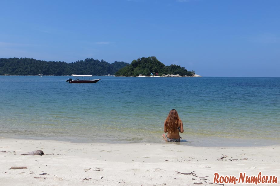 Девушка сидит на пляже и смотрит на море и необитаемый остров